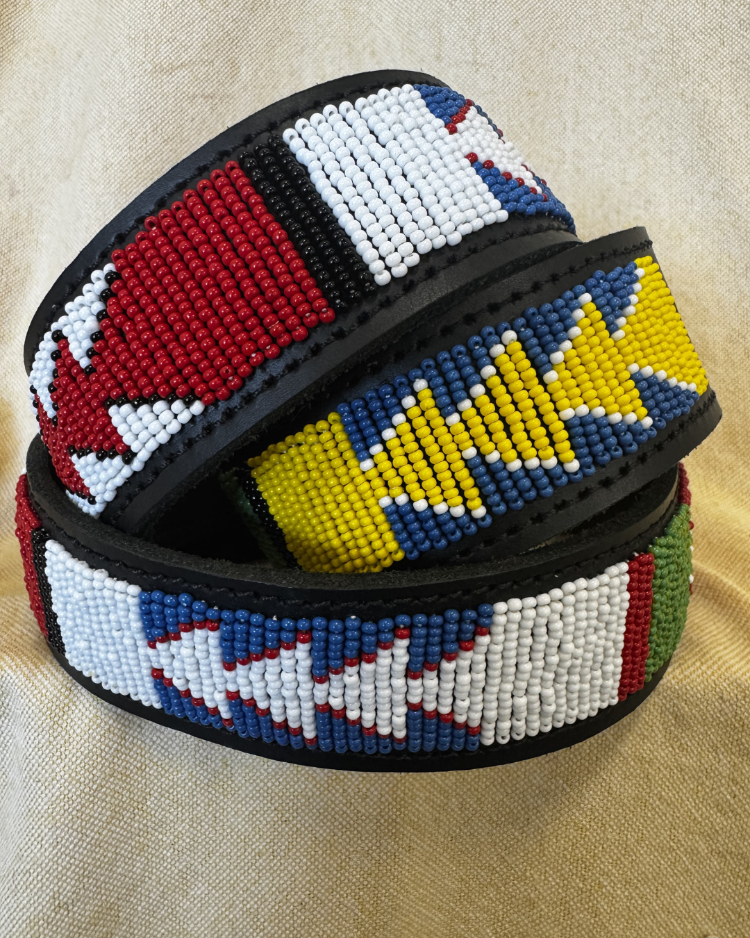 A coiled beaded belt with a black base and geometric beadwork in red, white, blue, yellow, and green, displayed on a beige textured fabric background.
